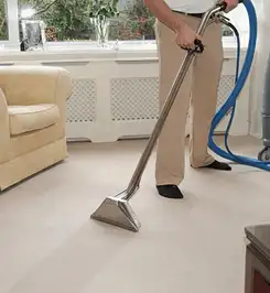 Professional carpet cleaner using a hot-water extraction wand and hose machine in a living room in Las Vegas, NV.