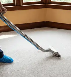 Steam carpet cleaning technician using a hot-water extraction wand on a residential carpet, wearing blue protective shoe covers Las Vegas, NV.