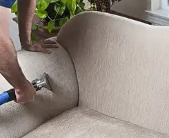 Professional upholstery cleaner deep-cleaning a fabric sofa with a handheld extraction tool and hose in Las Vegas, NV.